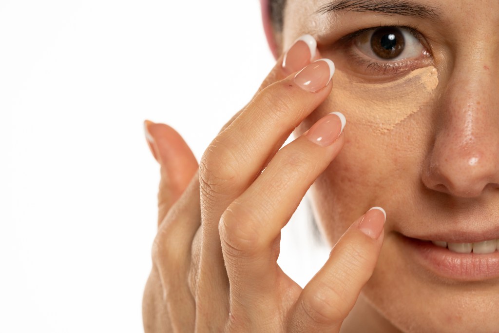 Middle-aged woman applying concealer under her eyes on a white background